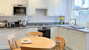 Een moderne keuken met witte kasten, een houten eettafel en stoelen. Er is een raam met uitzicht op de omgeving.