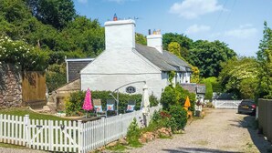 A quaint cottage with a white picket fence, a gravel driveway, and outdoor seating with umbrellas. - Bryn Euryn Cottage - 28135 (Rhos-on-Sea, near Colwyn Bay)