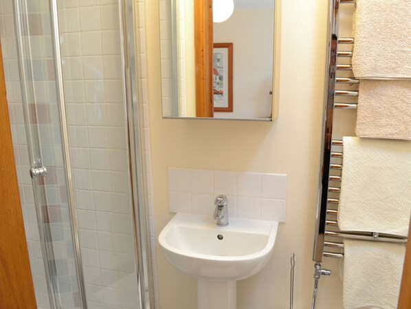 A bathroom with a glass shower enclosure, a white sink, and a towel rack with multiple towels.