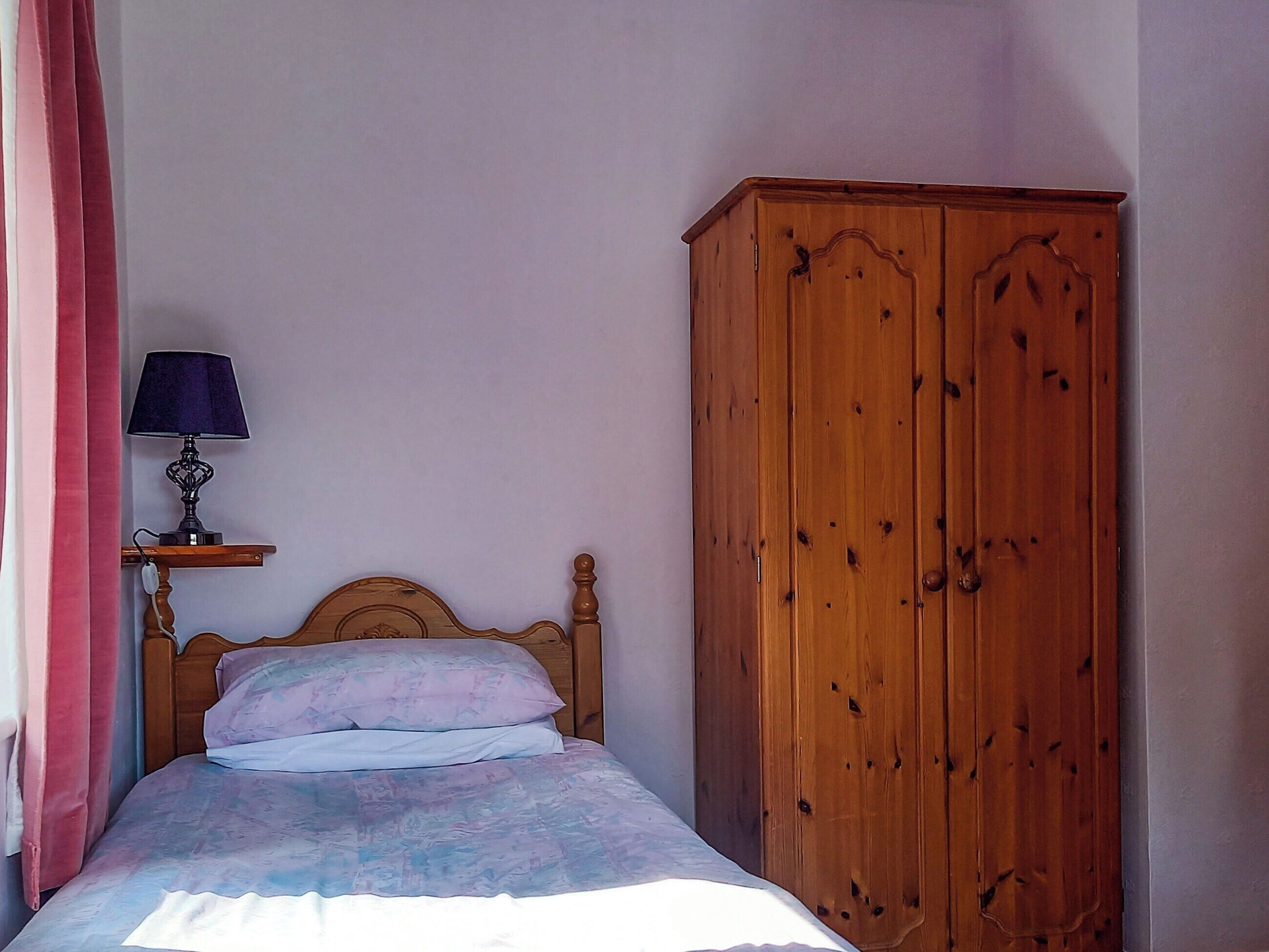 A bedroom with a wooden bed, a bedside table with a lamp, and a wardrobe.