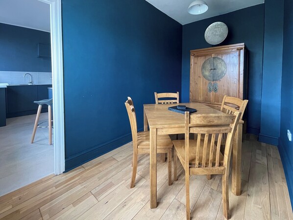 Ein Essbereich mit einem Holztisch und Stühlen, einem Holzschrank mit Verzierungen und einer Küche im Hintergrund.