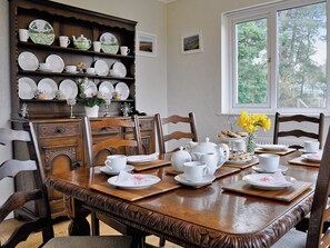 Une salle à manger avec une table en bois dressée pour le repas, entourée de chaises, et un buffet en porcelaine au-dessus.