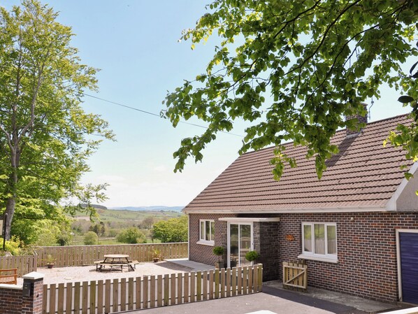 Une maison en briques avec un toit en tuiles, une clôture en bois et une terrasse avec une table et des chaises.