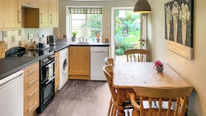 A compact kitchen with wooden cabinets, a washing machine, and a dining table with chairs. - 2 bedroom accommodation in North Chideock, near Bridport (North Chideock, near Bridport)