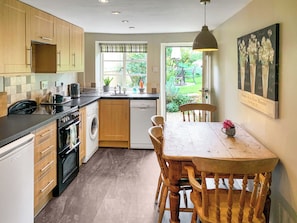 A compact kitchen with wooden cabinets, a washing machine, and a dining table with chairs.