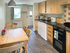 A kitchen with wooden cabinets, a black stove, a dishwasher, and a dining table with chairs.