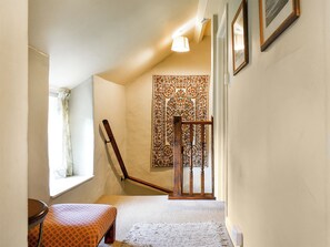 A narrow hallway with a patterned tapestry on the wall, a wooden chair, and a staircase with a wooden railing.