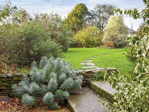 A garden with a stone pathway leading through lush greenery and a well-maintained lawn.
