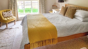 A bedroom with a large bed, a chair, a nightstand, and a lamp. - 2 bedroom accommodation in North Chideock, near Bridport (North Chideock, near Bridport)