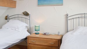 Quarto com duas camas de solteiro, mesa de cabeceira de madeira, luminária e quadro com cena de praia.