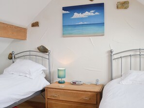 Un dormitorio con dos camas individuales, una mesita de noche de madera, una lámpara y un cuadro con una playa.