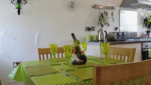 Uma área de refeições com toalha de mesa verde com bolinhas, cadeiras de madeira e uma garrafa de vinho na mesa.