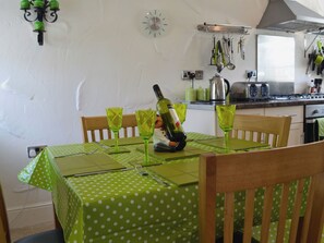 A dining area with a green polka dot tablecloth, wooden chairs, and a bottle of wine on the table.