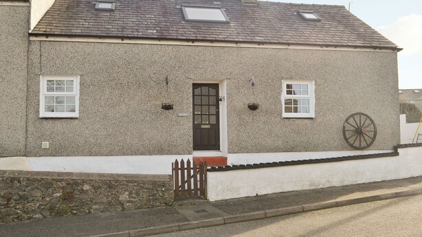Uma casa de dois andares com fachada de pedra, uma porta preta e uma pequena varanda com cerca de madeira.
