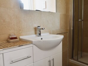 A bathroom with a white sink, a glass shower enclosure, and a tiled floor.