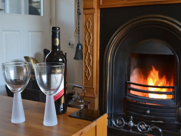 A bottle of Shiraz wine and two wine glasses on a wooden table with a fireplace in the background.
