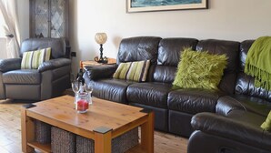 Uma sala de estar com um sofá de couro escuro, uma mesa de centro de madeira e um quadro na parede.