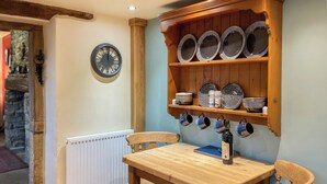 Una mesa de madera con sillas, un reloj en la pared y estantes con platos y cuencos.