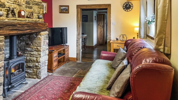Una sala de estar acogedora con chimenea de piedra, televisor, sofá de cuero y alfombra estampada.