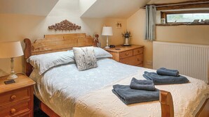 Un dormitorio con una cama grande, cabecera de madera, mesitas de noche con lámparas, una mesita auxiliar y una ventana con vistas.
