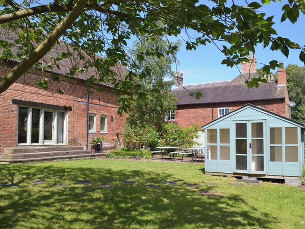 A brick building with a green-roofed shed, a lawn, and a tree.