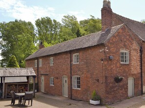 A brick building with a tiled roof, a small outdoor seating area, and a window with a white frame.