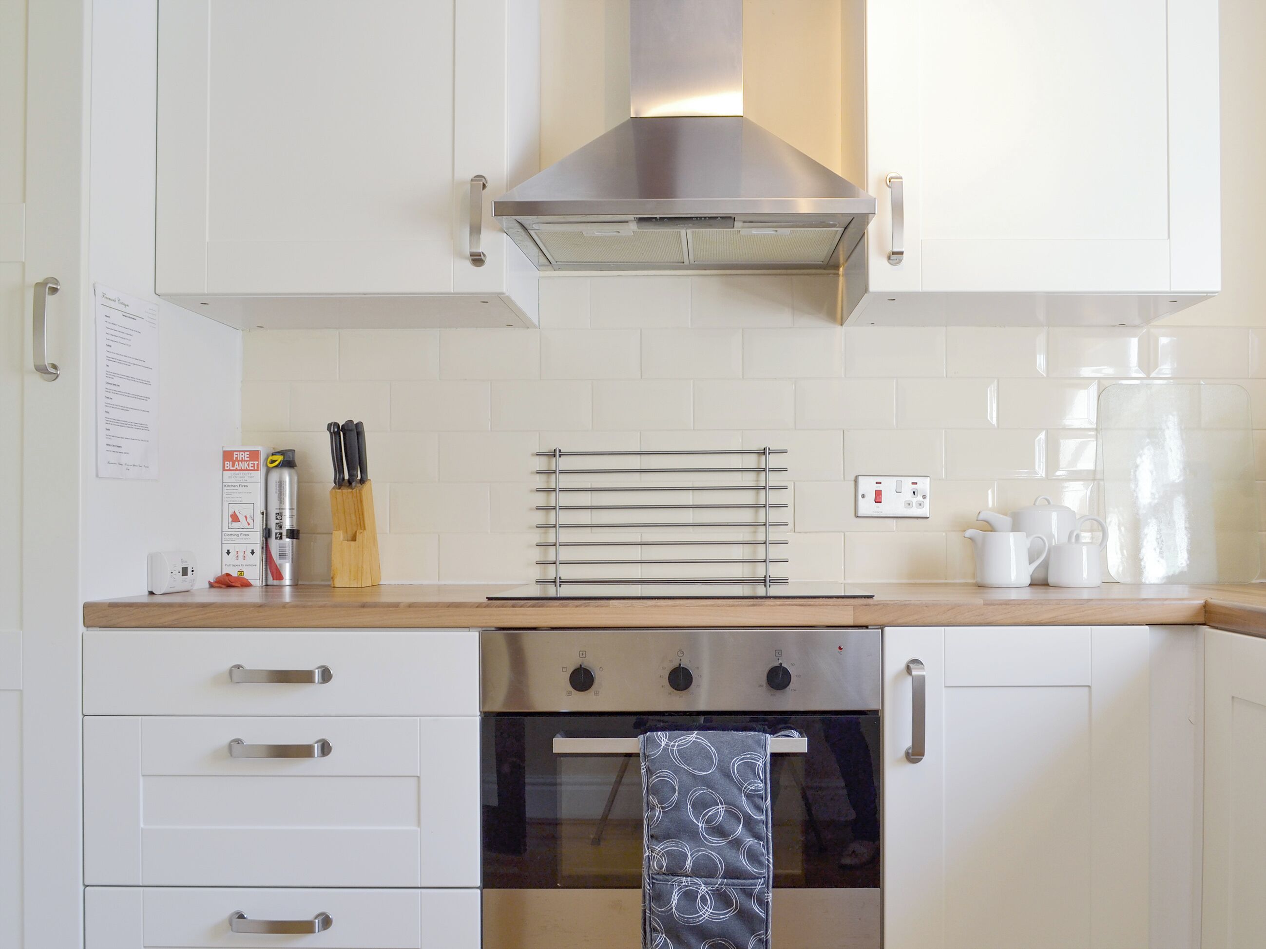 A kitchen with white cabinets, a stainless steel range hood, a built-in oven, and a towel rack.
