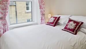 A bedroom with a large bed, two decorative pillows, a window with curtains, and a bedside lamp.