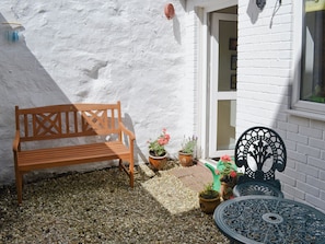 A wooden bench, potted plants, a metal table, and a white brick wall. - A period cottage within a short walk of Alnwick town centre. (Alnwick)