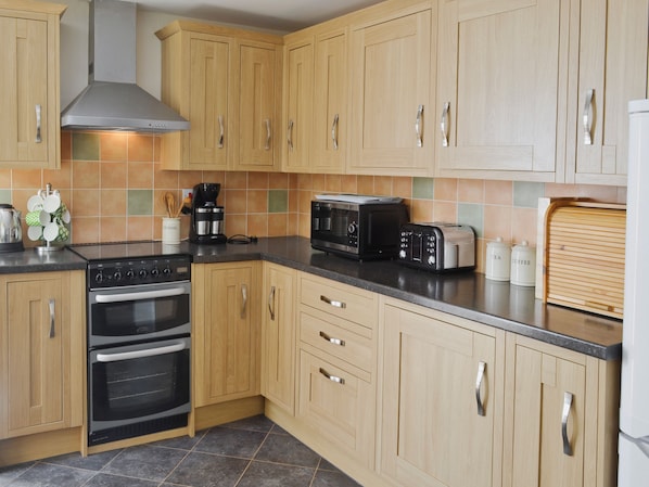 A kitchen with wooden cabinets, a stove, a microwave, a toaster, and a coffee maker. - A period cottage within a short walk of Alnwick town centre. (Alnwick)