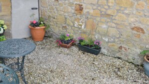 A stone wall with potted plants, a window, and a metal table.