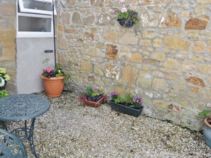 A stone wall with potted plants, a window, and a metal table. - A period cottage within a short walk of Alnwick town centre. (Alnwick)