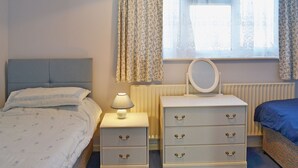A bedroom with a bed, a nightstand with a lamp, a dresser with drawers, and a window with curtains. - 2 bedroom accommodation in Hopton-on-Sea, near Great Yarmouth (Hopton-on-Sea, near Great Yarmouth)