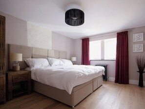 A bedroom with a bed, bedside tables, a window with curtains, and a radiator.
