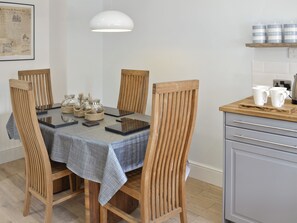 A dining area with a table set for four, surrounded by wooden chairs, a white pendant light, and a kitchen area with a wooden countertop and cabinets.