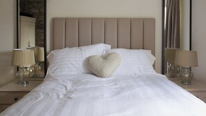 Un letto ben rifatto con lenzuola bianche, un cuscino a forma di cuore e due abat-jour.