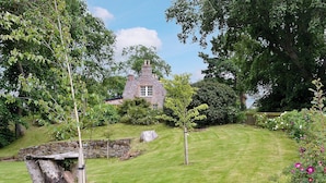 A stone house with a stone wall and a wooden bridge in a lush garden. - 4 bedroom accommodation in Bayfield, Nigg (Bayfield, Nigg)