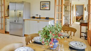 A dining area with a wooden table set for four, surrounded by chairs. A vase with green foliage and red flowers is placed on the table. - 4 bedroom accommodation in Bayfield, Nigg (Bayfield, Nigg)