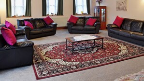 A living room with two black leather sofas, a coffee table, and a large patterned rug. - 5 bedroom accommodation in Uploders, Bridport (Uploders, Bridport)