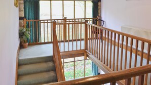 A staircase with wooden railings, a view of the outdoors through large windows, and a potted plant on the landing. - 5 bedroom accommodation in Uploders, Bridport (Uploders, Bridport)