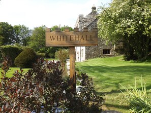 Une enseigne en bois portant l’inscription « WHITEHALL » est placée devant un bâtiment en pierre au style traditionnel, le tout étant entouré d’une végétation bien entretenue.