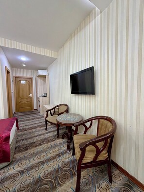 A hotel room with a television mounted on the wall, a small round table with chairs, a bed with a red cover, and a patterned carpet. - Royal Hotel (Baku)