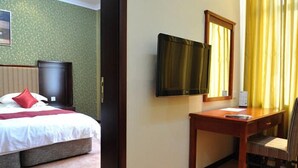 Habitació d'hotel amb un llit, escriptori, cadira, televisió i finestra amb cortines.