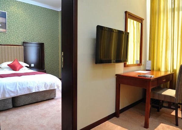 A hotel room with a bed, a desk, a chair, a TV, and a window with curtains.