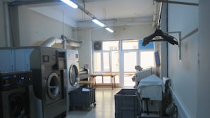 A laundry room with industrial washing machines, a drying rack, and storage bins. - Royal Hotel (Baku)