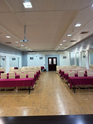 A conference room with rows of tables, chairs, and a projector on the ceiling. - Royal Hotel (Baku)