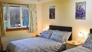 Een slaapkamer met twee bedden, een raam met gordijnen, een radiator en een wandlamp.