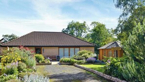 Een tweelaags huis met pannendak, omgeven door een verzorgde tuin met verschillende planten en bloemen.
