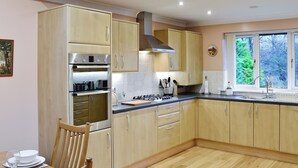 Een moderne keuken met houten kastjes, roestvrijstalen apparatuur en een eethoek met een tafel voor twee personen.