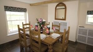 A dining area with a wooden table set for four, surrounded by chairs. There is a vase with flowers on the table, and a mirror on the wall above it. - Somer Leyton Cottage (Hogsthorpe, near Chapel St Leonards)
